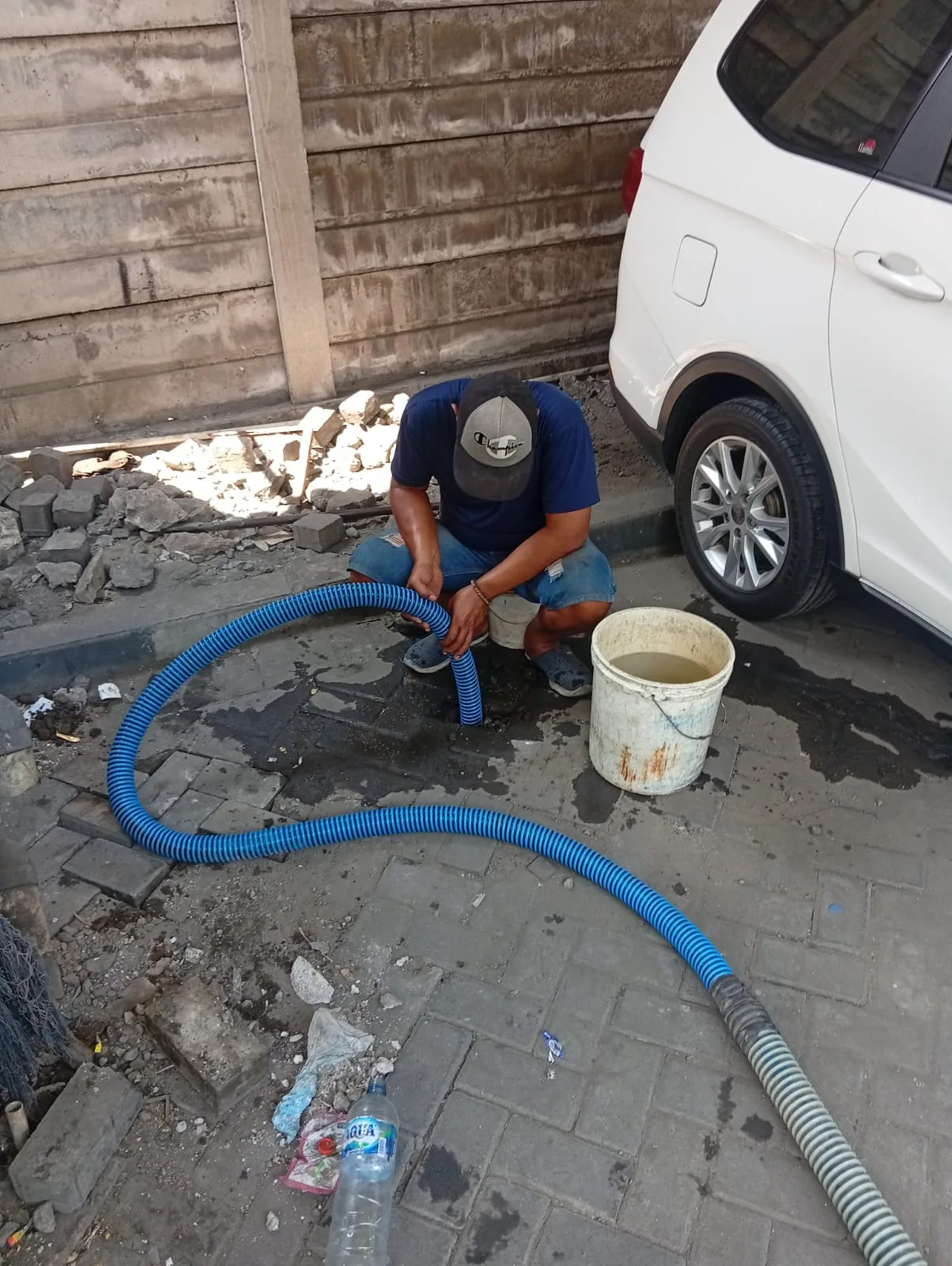 Petugas menyedot septic tank melalui akses di halaman dekat sebuah mobil.