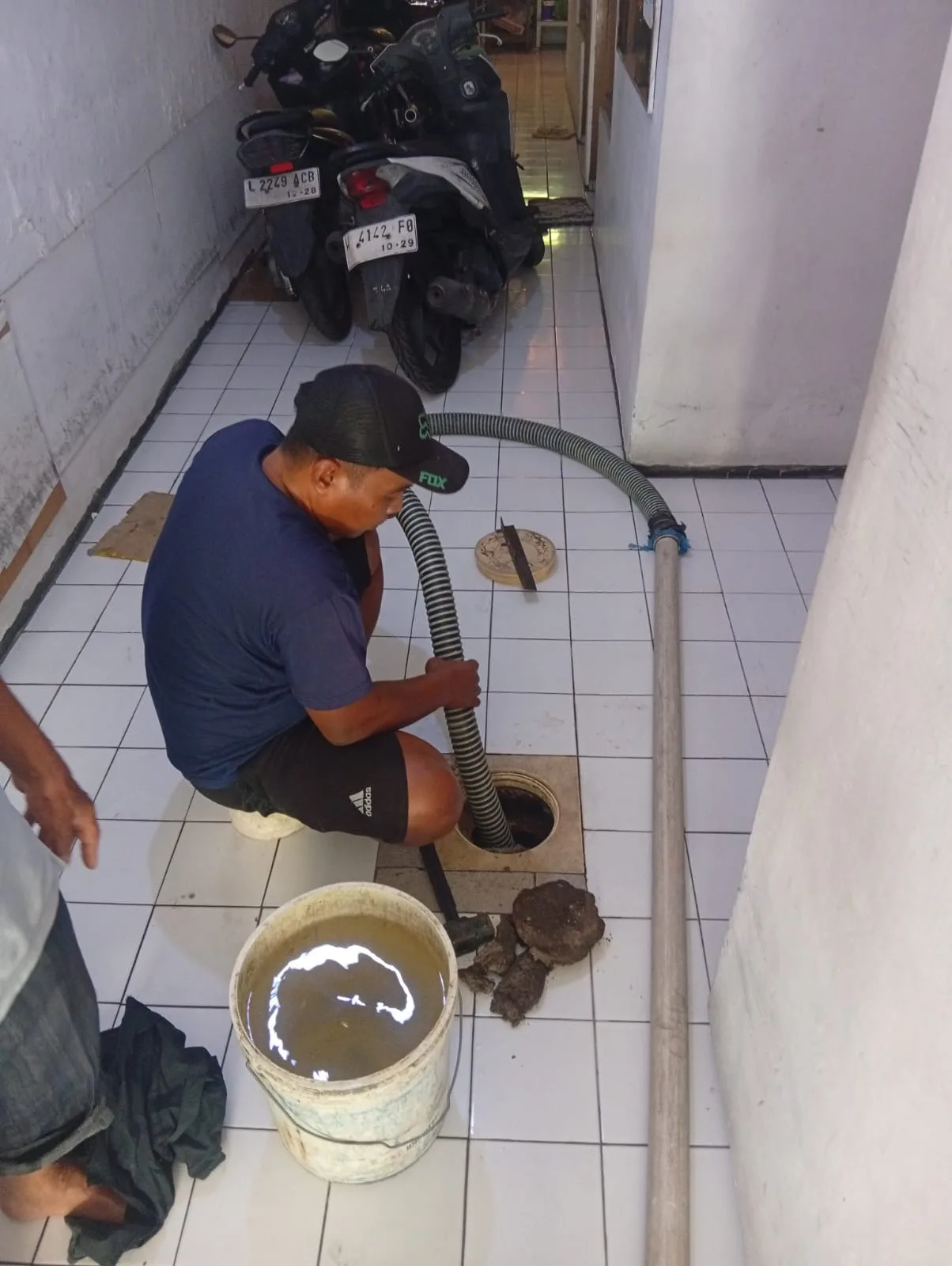 Petugas menggunakan selang untuk menyedot septic tank di dalam ruangan.