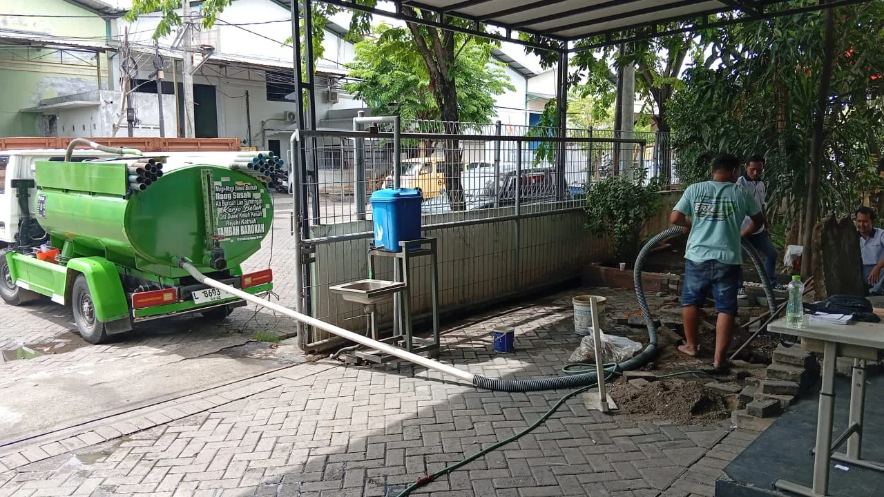 Petugas mengatur selang dari truk tangki di area bangunan.